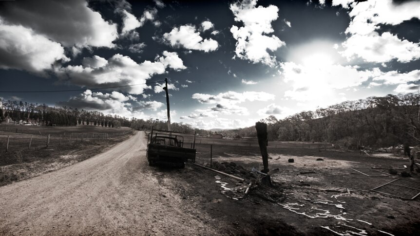 A panorama view of the Ogilvie's driveway, with a burnt car and paddocks.