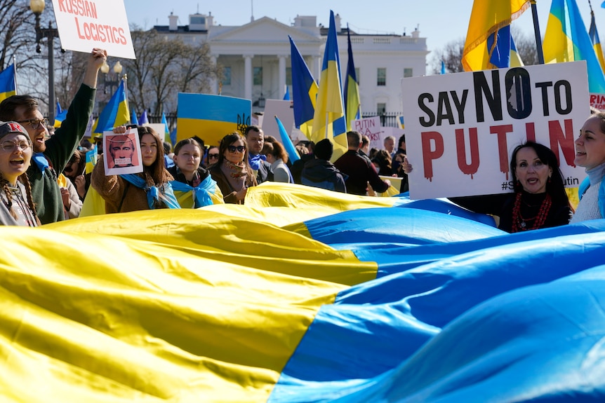 A crowd hold a large banner of the Ukrainian flag, smaller flags and banners outside the White House in Washington DC