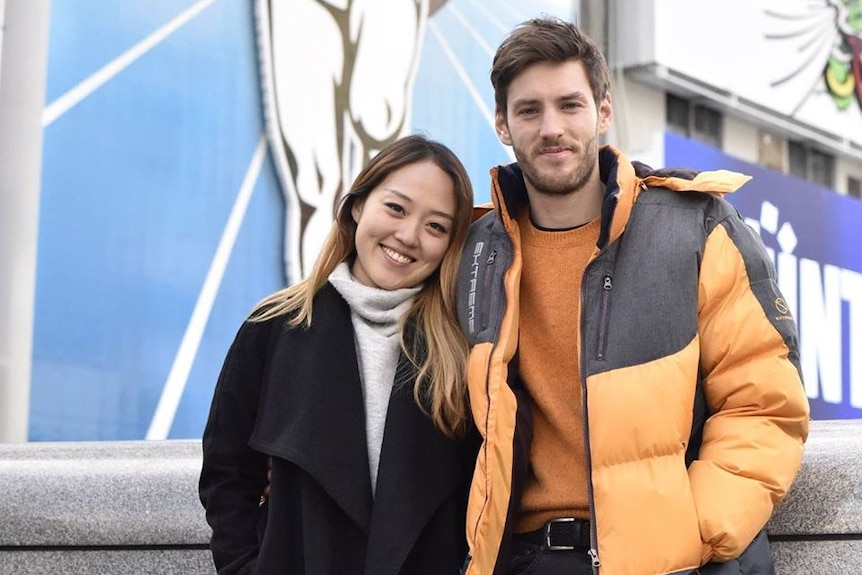 A woman affectionately leans her head against a man wearing a yellow jacket.