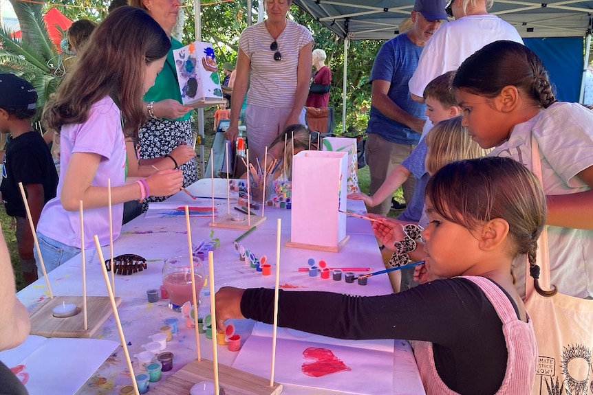 Children are gathered around a table making candles on a wooden stand