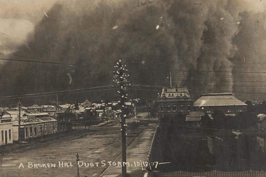 A small town with a billowing dust cloud in the distance