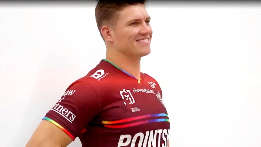 A man standing and smiling in a colourful jersey 