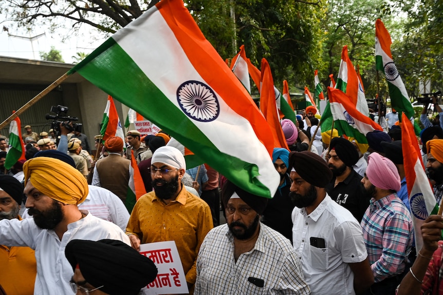 A crowd of people, mostly men in turbans, waving Sikh flags during a street protest