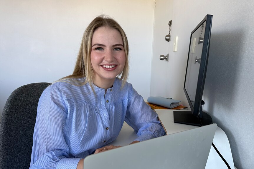 Naomi Lewis smiles while sitting at a desk with a computer.