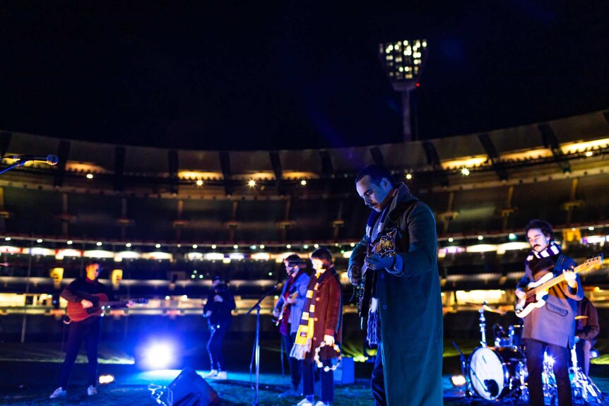 A band all wearing scarfs performing in the middle of the empty Melbourne Cricket Ground.