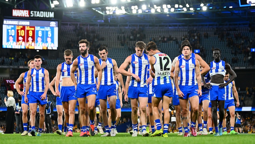 An AFL team in blue and white strips, walking off the field together, looking disappointed following a loss