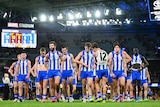 An AFL team in blue and white strips, walking off the field together, looking disappointed following a loss