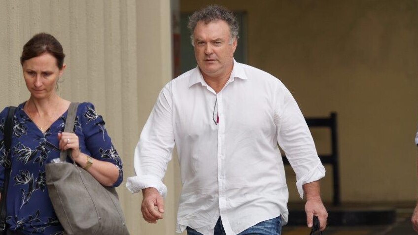 Rod Culleton wearing a white shirt walking next to a woman on a footpath outside a court building.