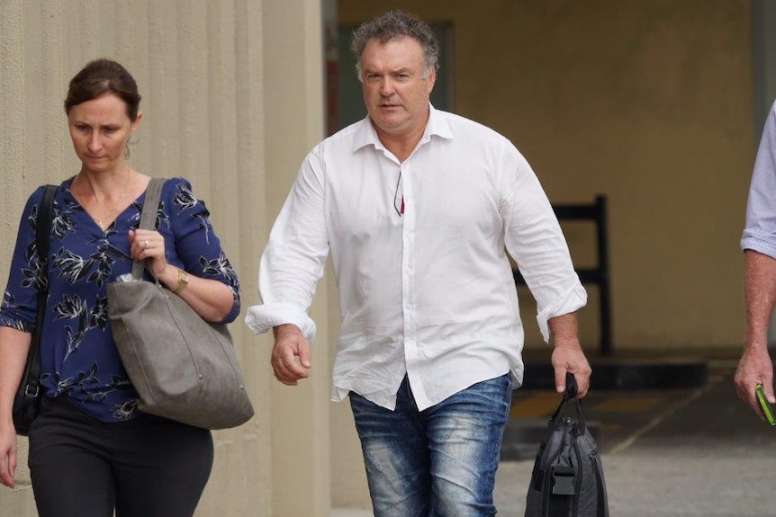 Rod Culleton wearing a white shirt walking next to a woman on a footpath outside a court building.