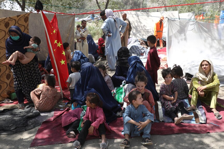 A group of people sitting among pieces of fabric, as makeshift shelters in a park