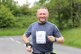 Gary McKee running along a road during the day smiling and looking toward the camera