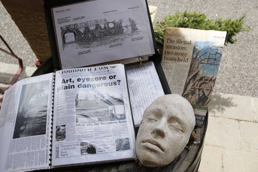 A collection of newspaper clippings and sketches about the Dreamers Gate artwork in Collector arrange on the top of a barrel.