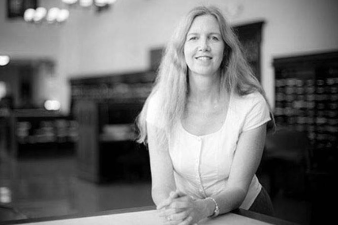 Professor Pamela Scully folds arms on a table she sits at, smiling. She has long, fair hair.