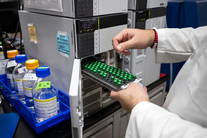 A scientist prepares a series of samples to be placed into a machine, while wearing a lab coat. 