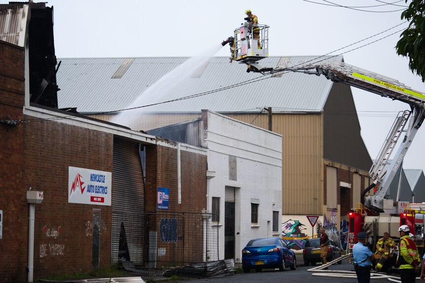 Firefighter with a hose on a cherry-picker crane douses a fire site.