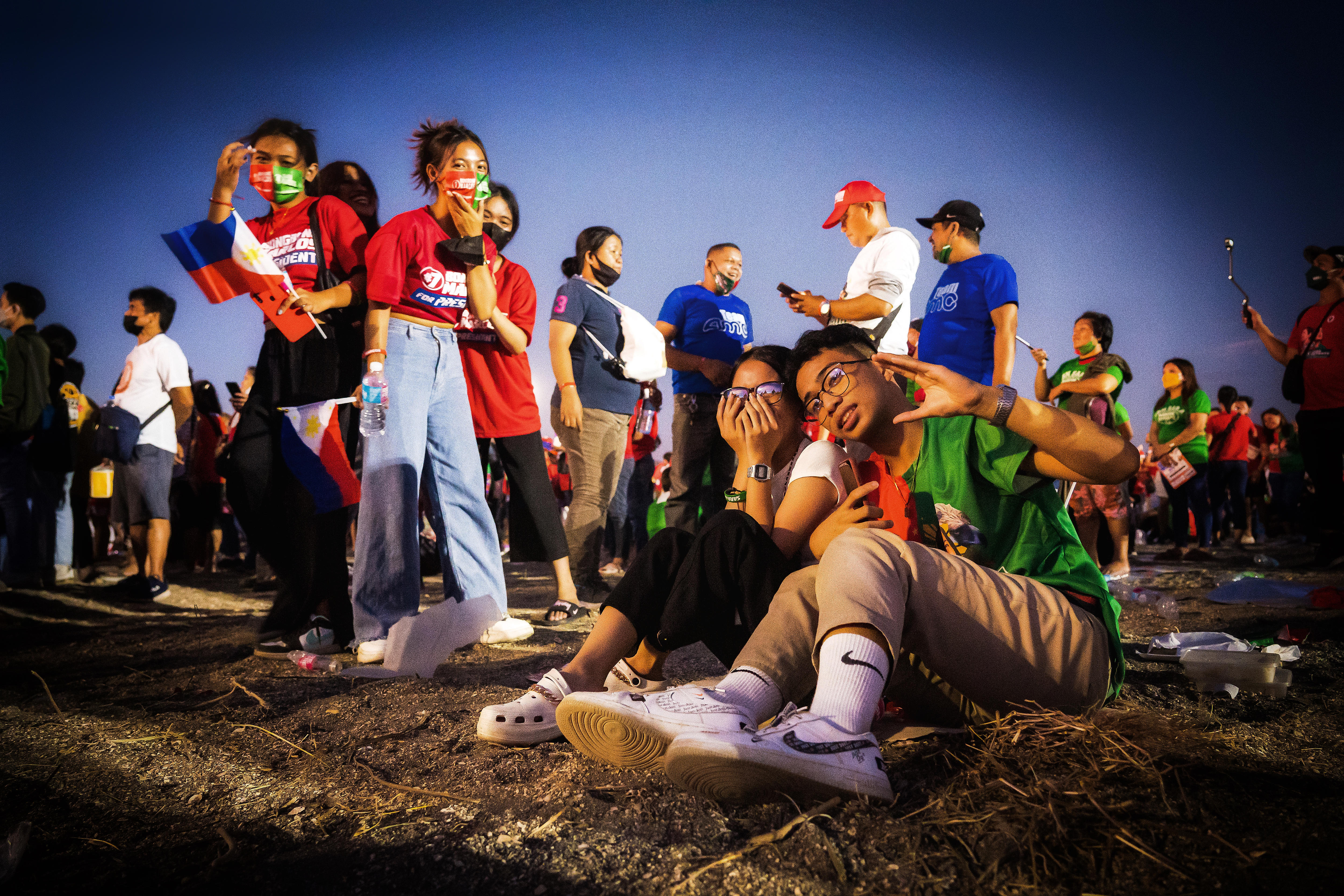 A group of young people sitting, standing and walking around a field. They wear political slogan shirts and masks