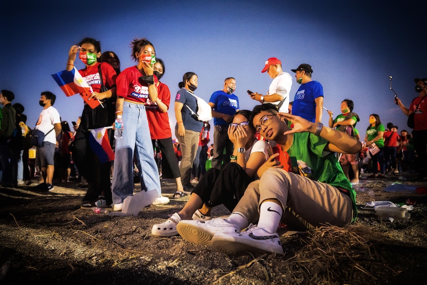 A group of young people sitting, standing and walking around a field. They wear political slogan shirts and masks