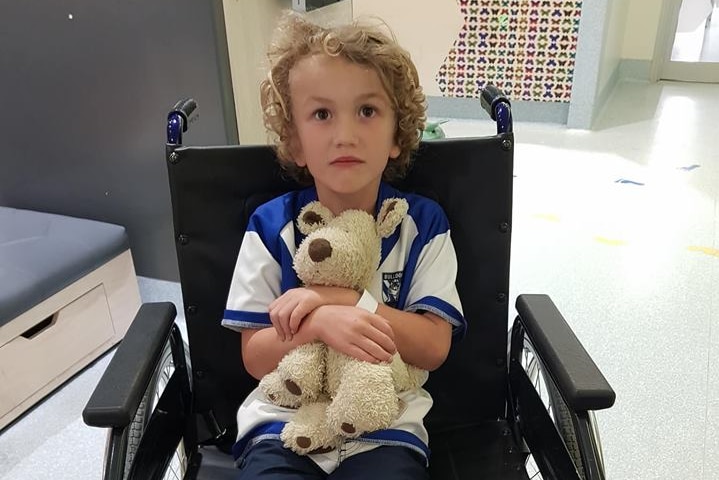 Kai Dight in wheelchair hugging teddy bear with bandages on his feet.