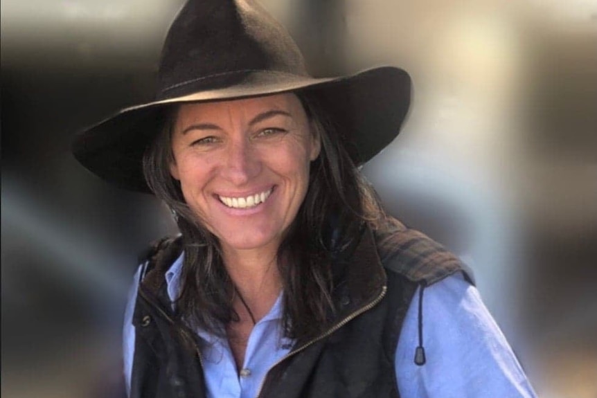 A woman with a broad brimmed hat smiles at the camera