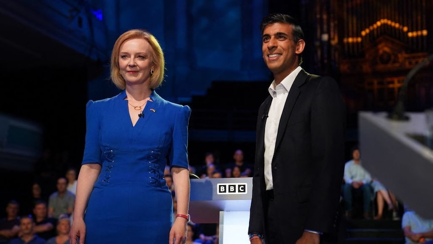 Liz Truss dressed in a blue dress and Rishi Sukin in a dark suit with no tie smile for the camera in front of a BBC podium