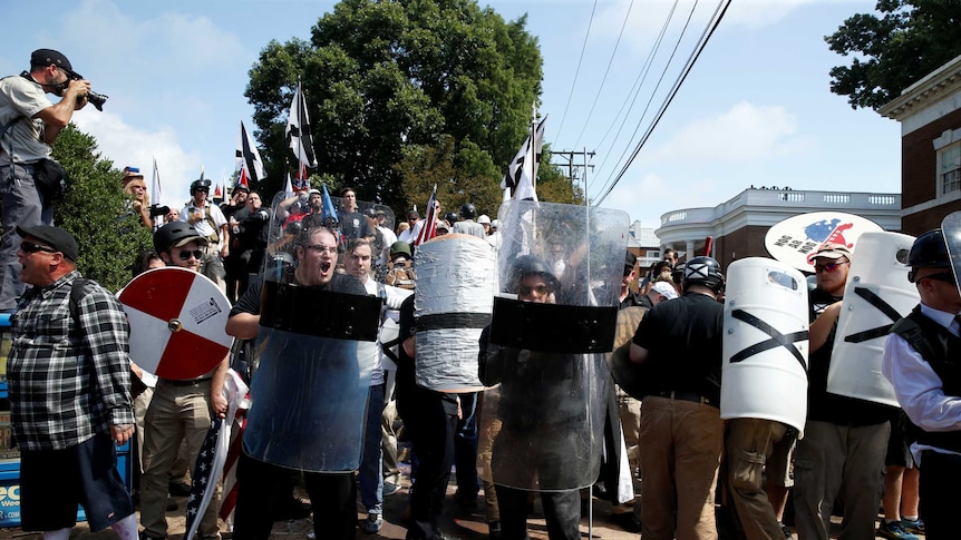 White nationalists hold plastic shields and carry black and white flags.