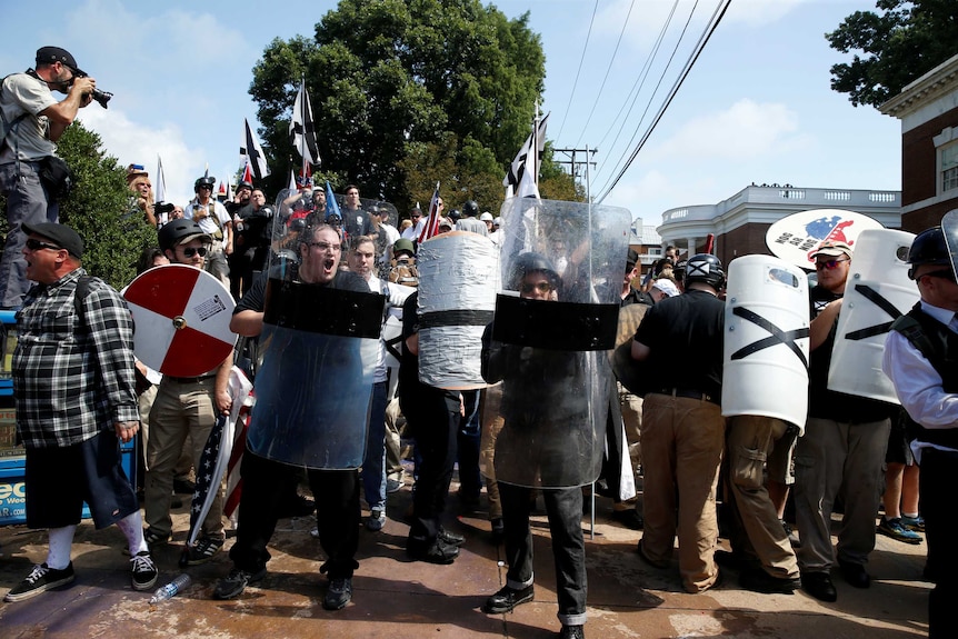 White nationalists hold plastic shields and carry black and white flags.