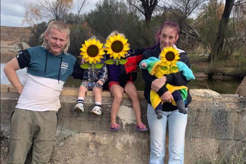 A couple in their twenties with their three young children who have sunflowers over their faces