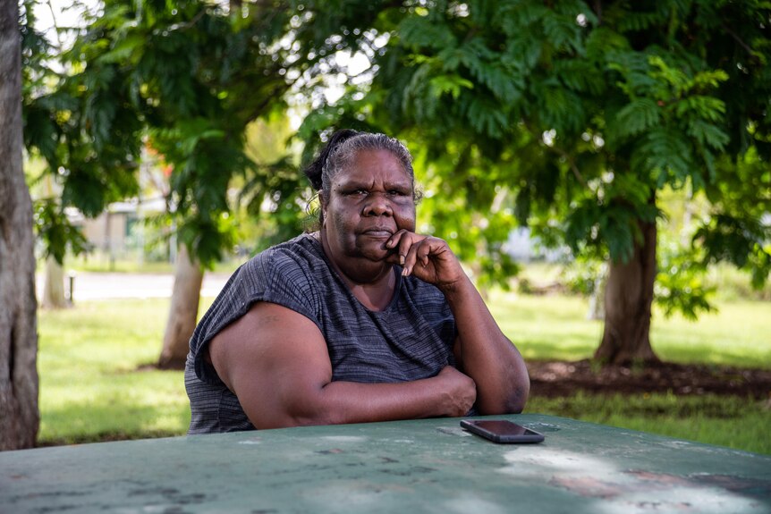 An Indigenous woman sitting at a park bench looking at the camera.