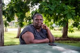 An Indigenous woman sitting at a park bench looking at the camera.