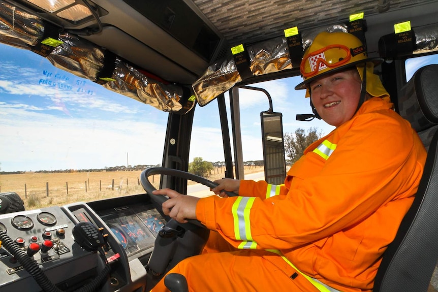 Woman in orange overalls and wearing yellow helmet at wheel of a fire truck
