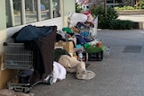 A man lies on the footpath surrounded by some shopping trolleys full of his possessions