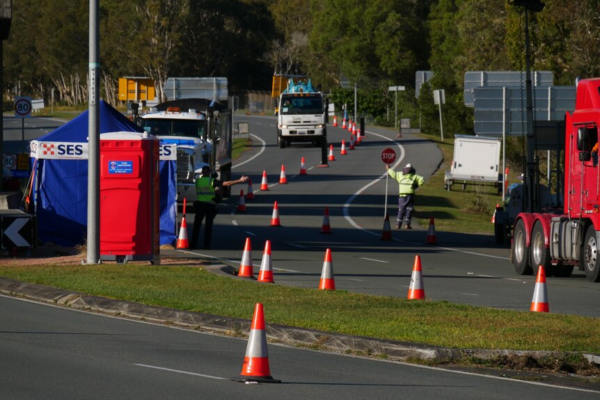 A road with traffic cones, an SES tent and a man with a stop sign