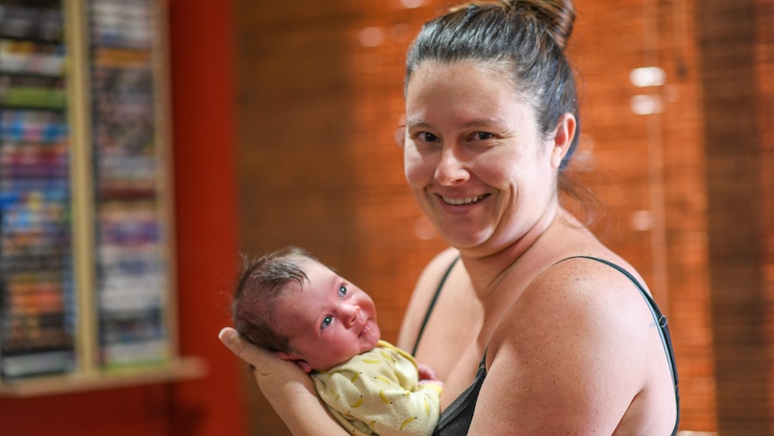 A woman in a black singlet smiles while holding a baby.