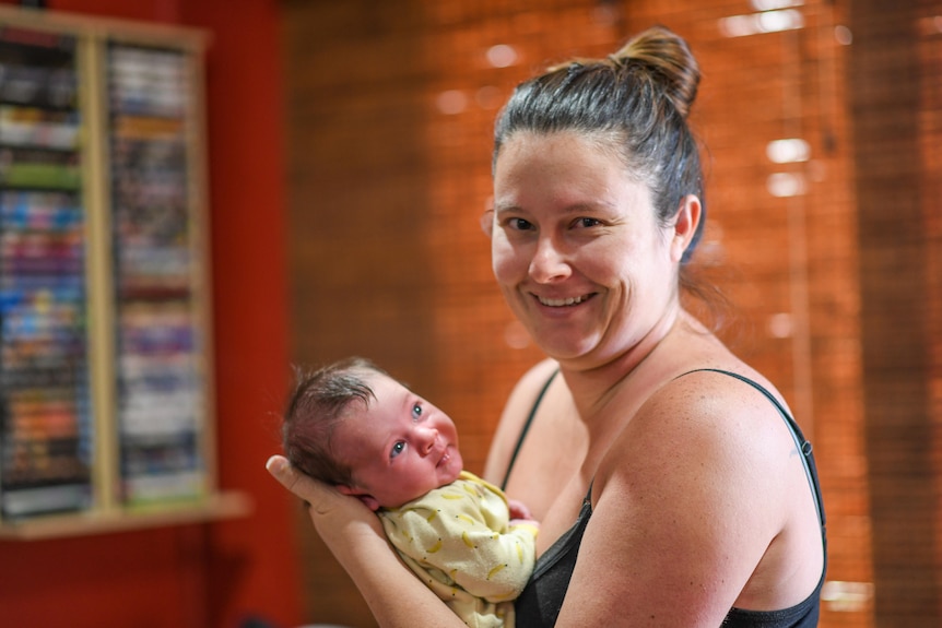 A woman in a black singlet smiles while holding a baby.