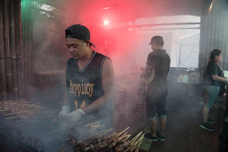 A vendor prepares food on a barbecue.