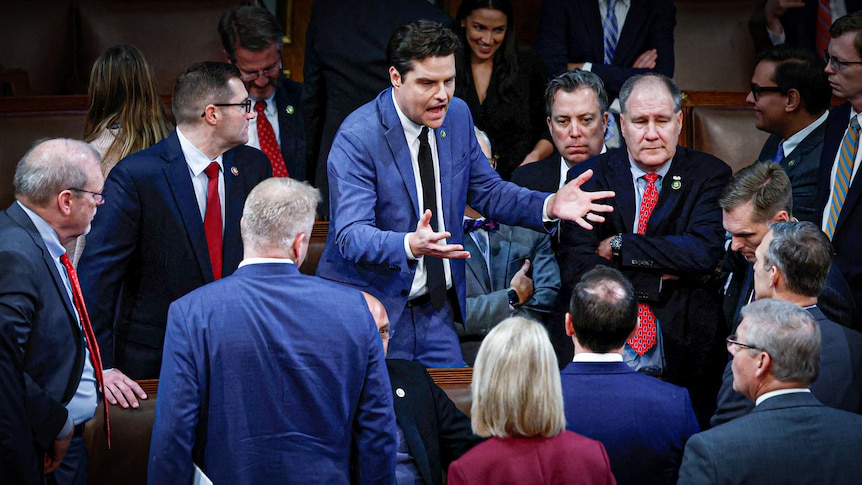 Matt Gaetz gesticulates while surrounded by men in suits 