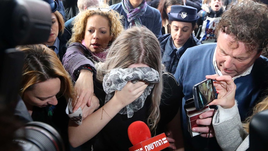 A woman covering her face with a scarf while she is surrounded by media.