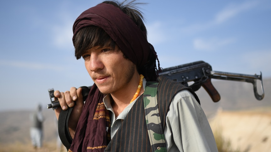 A young boy stands with a rifle across his back. 