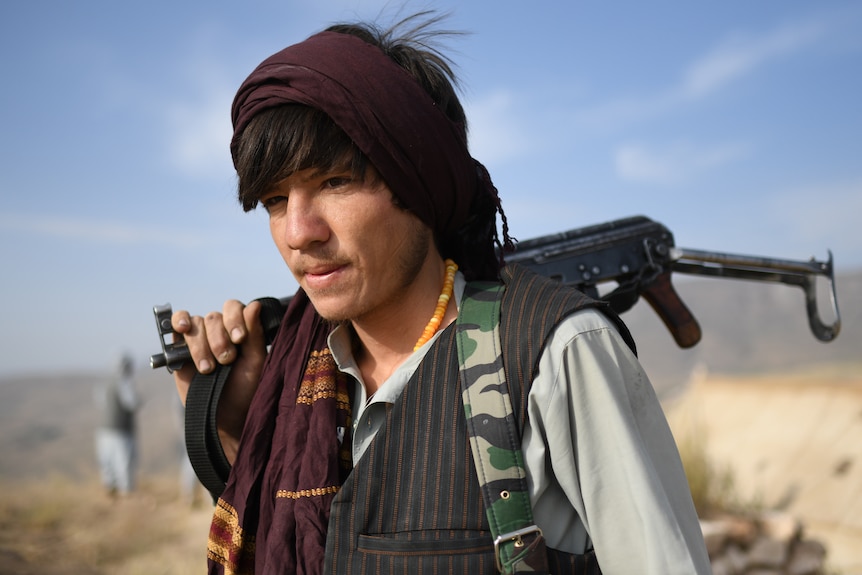 A young boy stands with a rifle across his back. 