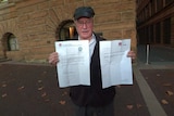 A man standing outside a hotel holding two pieces of paper.