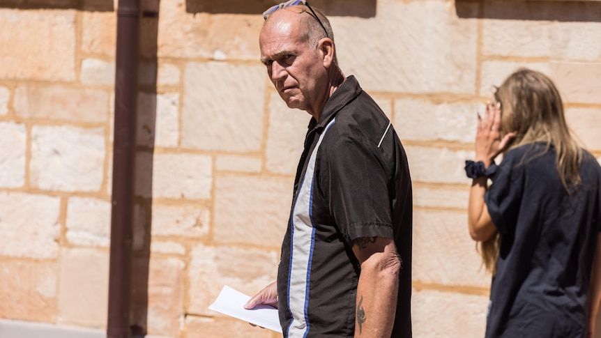 A man walking outside a courthouse while a female supporter shields her face.  