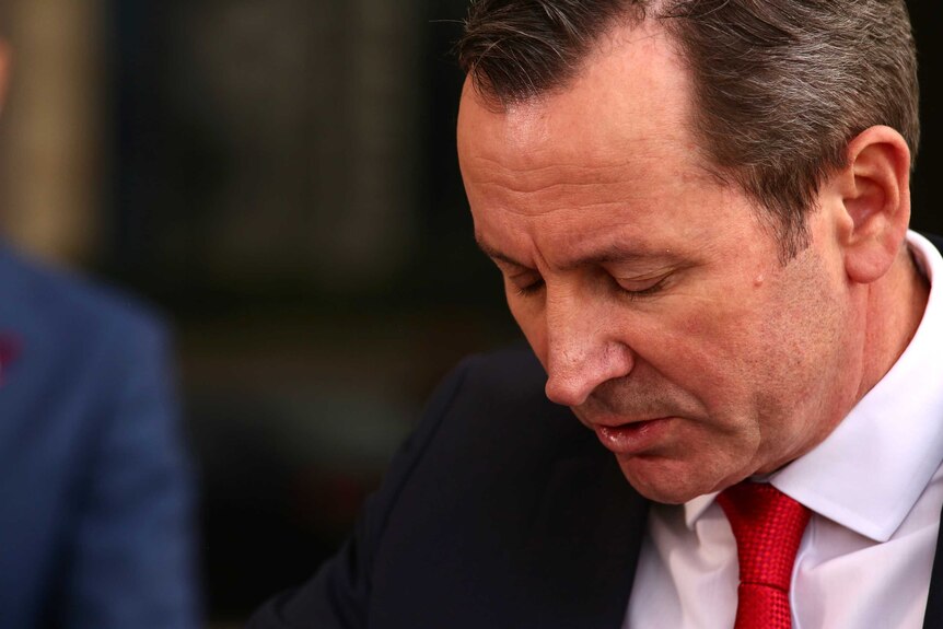 WA Premier Mark McGowan looks down disappointedly, wearing a red tie, a white shirt and a black suit