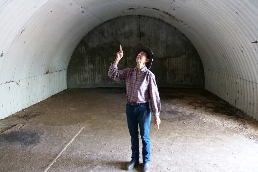 A woman stands in the middle of an underground bunker pointing at the curved roof
