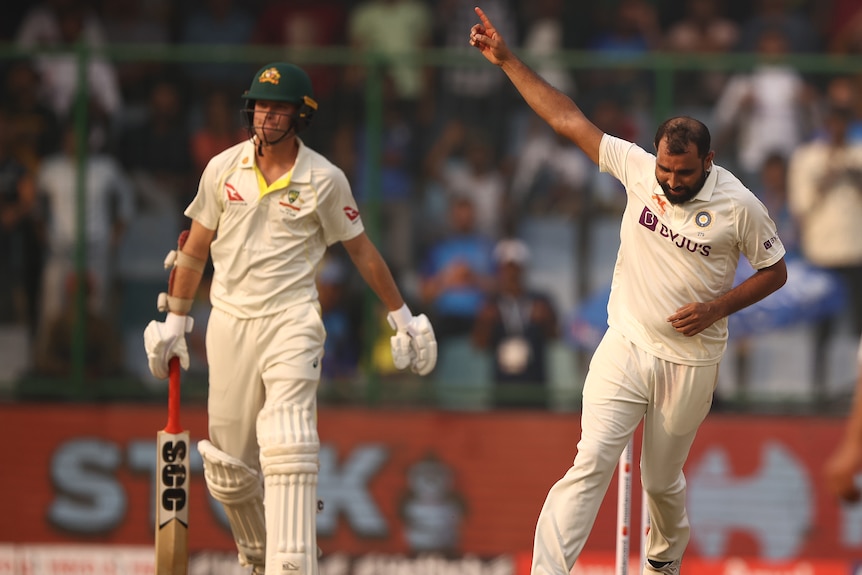 An Indian male Test bowler celebrates taking the wicket of Australia batter, who stands in the background.