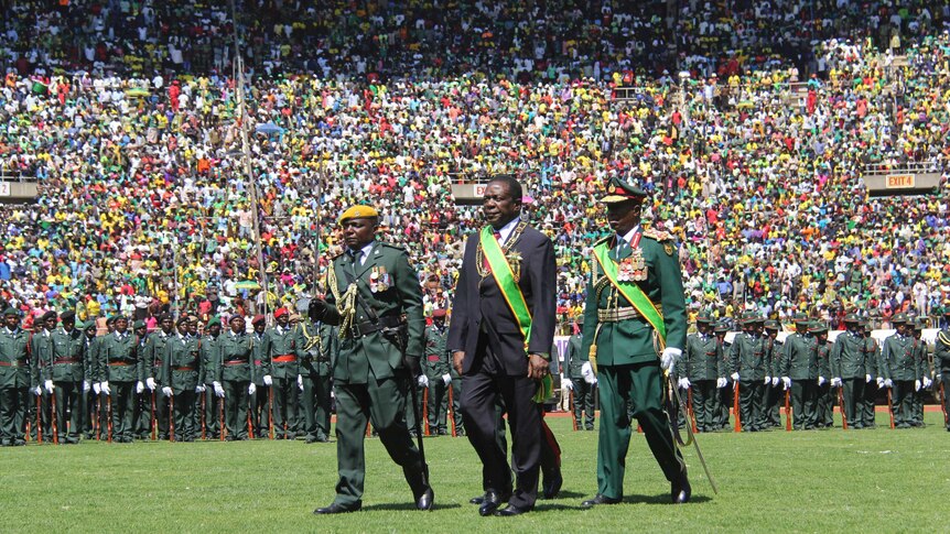 President Emmerson Mnangagwa inspects a guard of honour with huge crowds in the stadium behind him.
