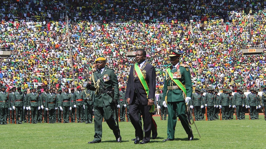 President Emmerson Mnangagwa inspects a guard of honour with huge crowds in the stadium behind him.