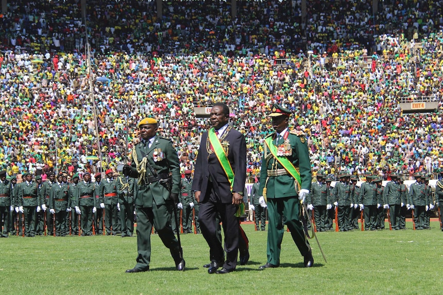 President Emmerson Mnangagwa inspects a guard of honour with huge crowds in the stadium behind him.