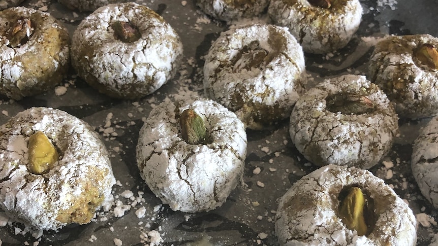 A baking tray of icing sugar encrusted baked cookies with a pistachio.