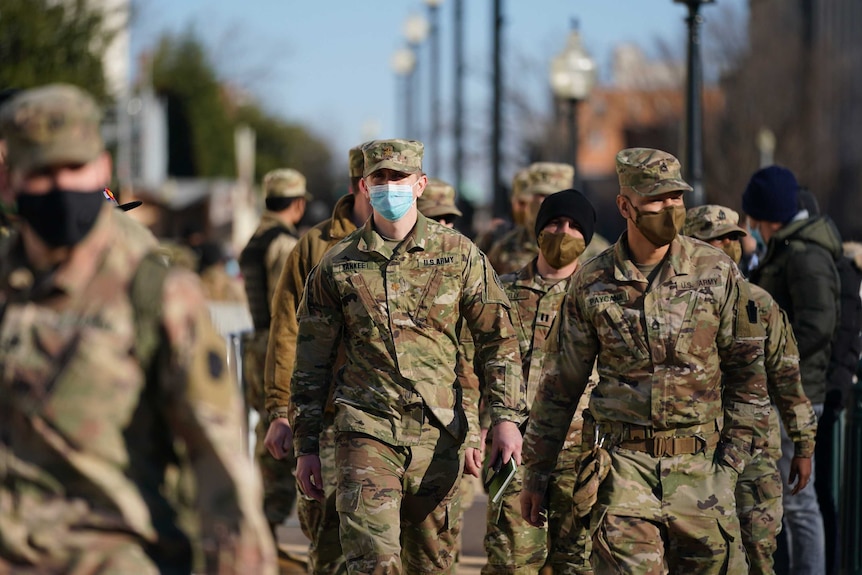 Un grupo de soldados con uniformes del ejército, sombreros y máscaras marchan juntos en una calle de Washington.