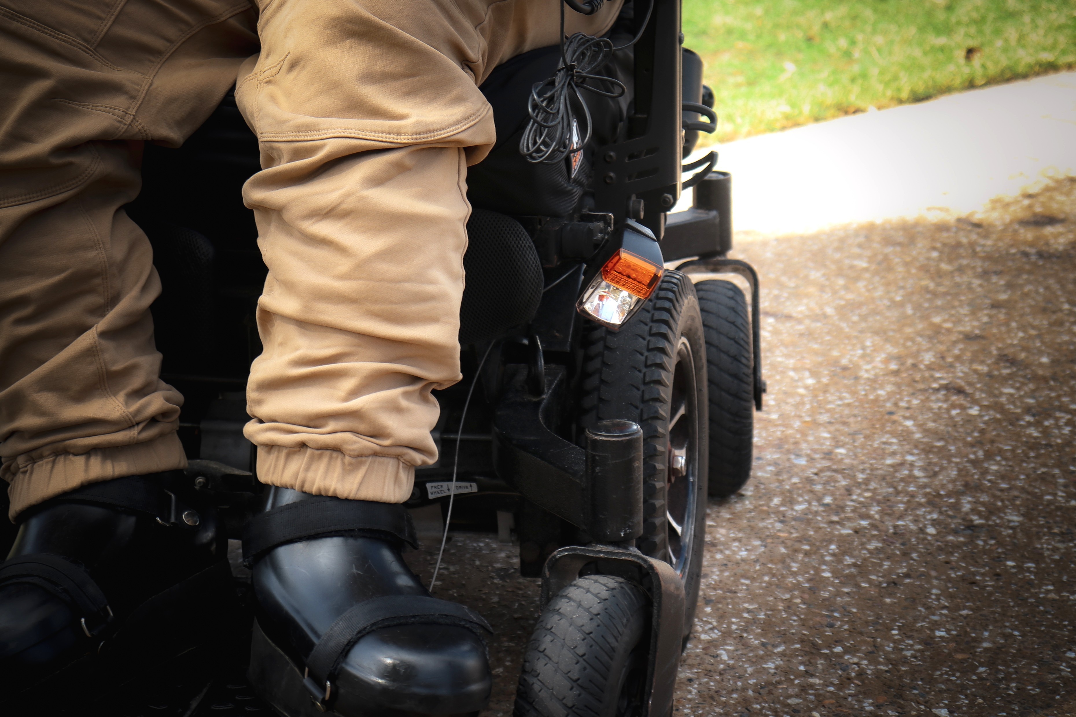 A man in a wheelchair. The photo is a close up of the man's legs and the wheels of his wheelchair.